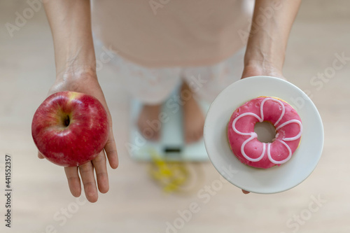 Women are choosing the right food for good health. Women are fasting. Comparison options between donuts and apples during weight measurement on digital scales. Diet concept.