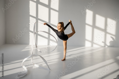 Canvas Print Little girl practising rhythmic gymnastics with a gymnastic tape at white sunny dance room