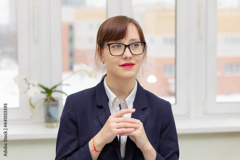 young stylish pretty business woman in a blue jacket and glasses by the window in the office at her workplace is satisfied with the work done young stylish pretty business woman in a blue jacket and glasses by the window in the office at her workplace is satisfied with the work done