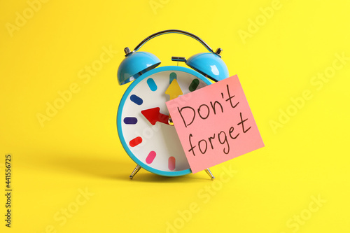 Alarm clock and reminder note with phrase Don't forget on yellow background photo