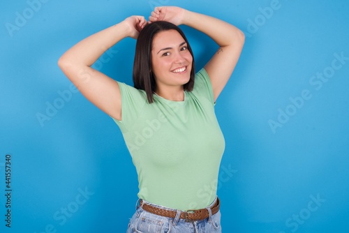 young beautiful brunette girl with short hair standing against blue background stretching arms, relaxed position.