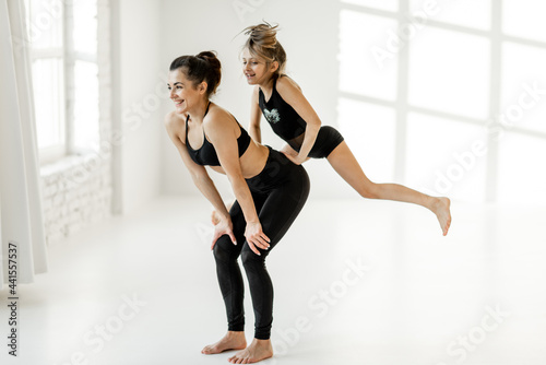 Happy sports mom or trainer with a little girl during gymnastics training  jumping and having fun at white classroom