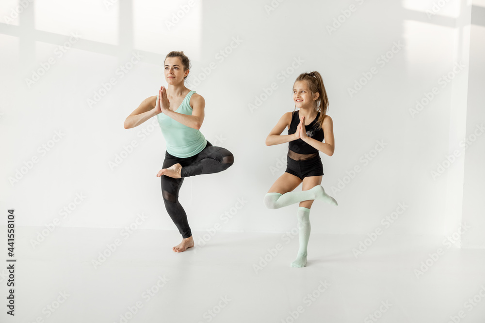 Fototapeta premium Young mom or sports coach trains little girl in rhythmic gymnastics at white sunny sport classroom. Individual sports lesson for children
