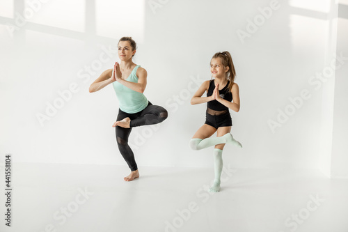 Young mom or sports coach trains little girl in rhythmic gymnastics at white sunny sport classroom. Individual sports lesson for children