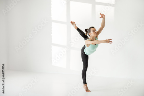 Athletic woman practising rhythmic gymnastics or ballet dance at white classroom alone