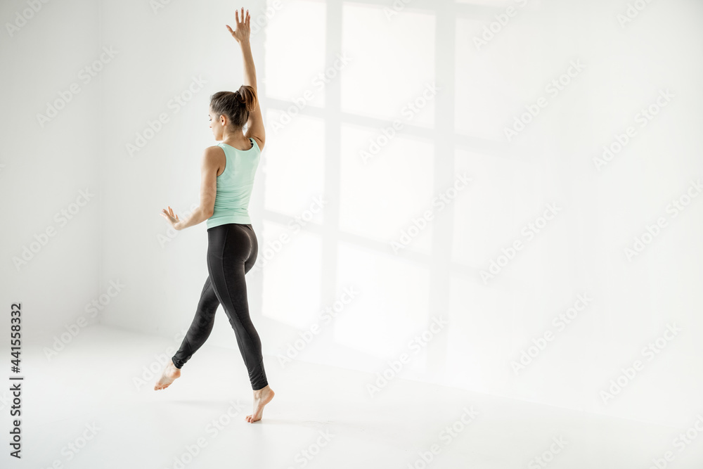 Athletic woman practising rhythmic gymnastics or ballet dance at white classroom alone Athletic woman practising rhythmic gymnastics or ballet dance at white classroom alone
