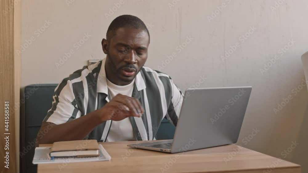 Dollying-out medium shot of successful young Afro American businessman having video conference with partners via laptop sitting at cafe table Dollying-out medium shot of successful young Afro American businessman having video conference with partners via laptop sitting at cafe table