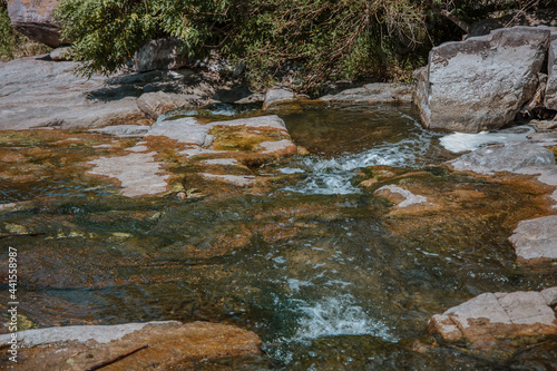 Selective focus close-up of clear stream water running over large rocks. Water running through a parkland during the daytime. Water runs through the stones summer time