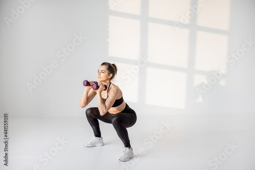Beautiful and confident athletic woman doing cardio with dumbbells at white room. Training fitness or aerobics alone © rh2010