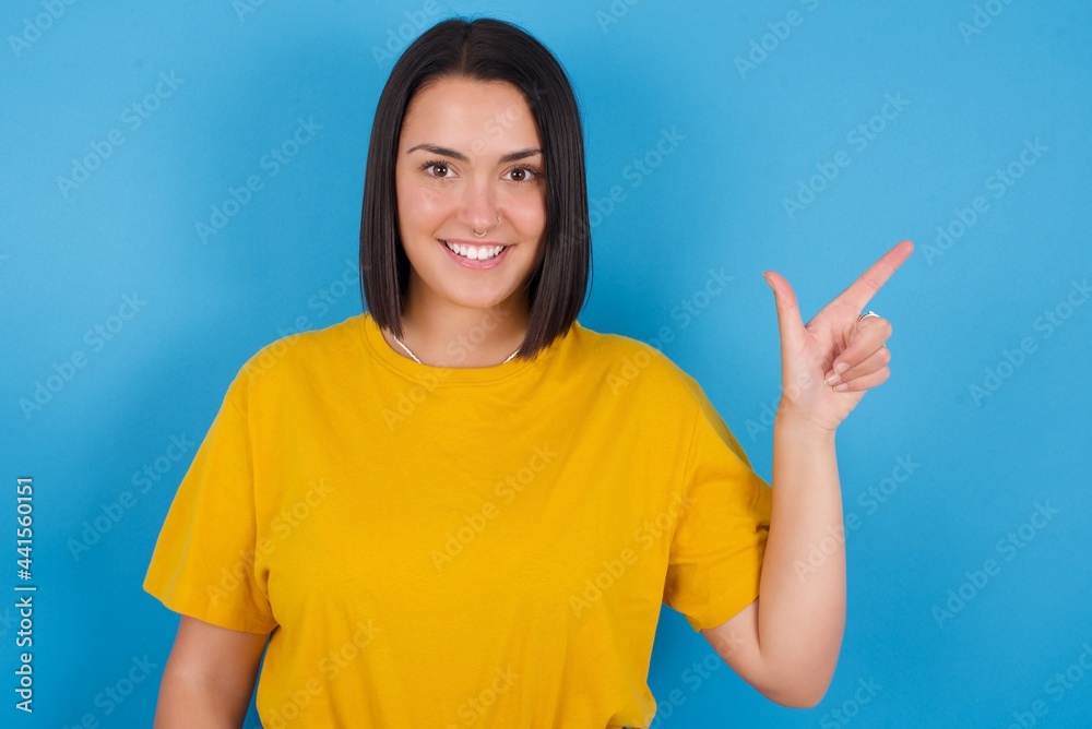 young beautiful brunette girl with short hair standing against blue background pointing up with fingers number eight in Chinese sign language BÄ. young beautiful brunette girl with short hair standing against blue background pointing up with fingers number eight in Chinese sign language BÄ.