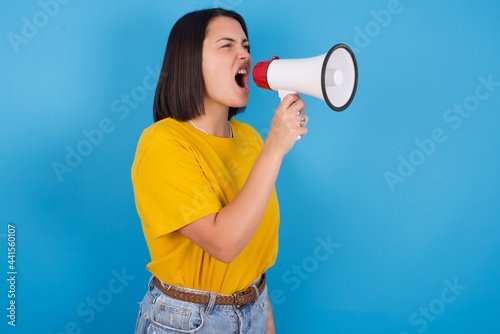 young beautiful brunette girl with short hair standing against blue background Through Megaphone with Available Copy Space