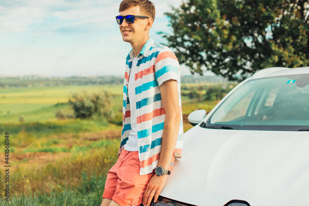 Young male enjoying the beautiful landscape while driving his car, a man standing near his car