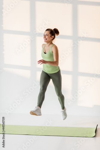 Portrait of a cheerful athletic woman in motion dressed in green sportswear during a sportbreak at fitness classroom