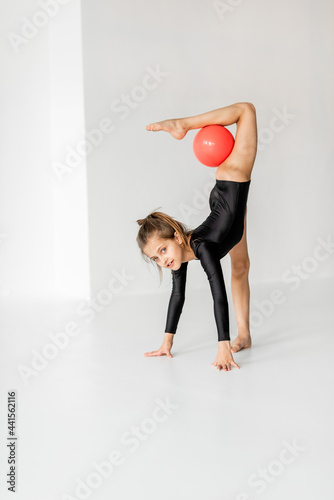 Little girl practising rhythmic gymnastic with a ball at white room. Children's gymnastics and training from an early age