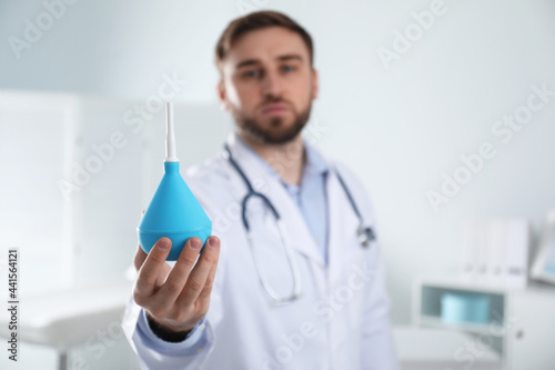 Doctor holding rubber enema in examination room, focus on hand. Space for text