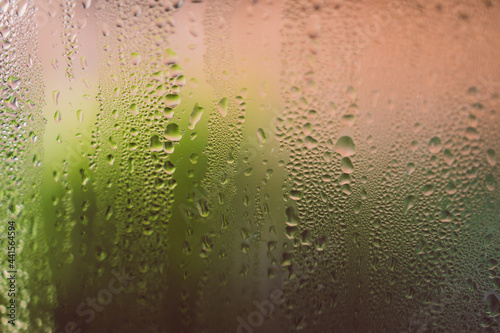 water droplets of humidity condensation on window seen from indoor with backyard bokeh in the background