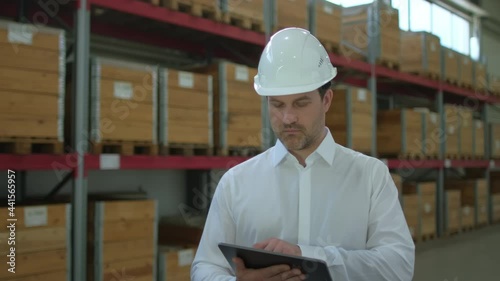 Employee male warehouse worker engineer man in hard hat working at construction site warehouse, walking in logistics center factory, storekeeper using tablet computer, architect businessman indoors