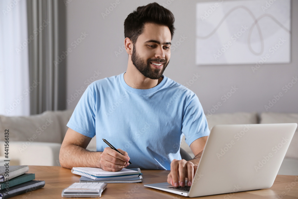 Young man watching webinar at table in room Young man watching webinar at table in room