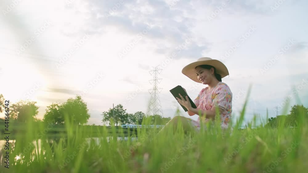 Asian woman using portable device sitting on lawn near river. Asian woman using portable device sitting on lawn near river.