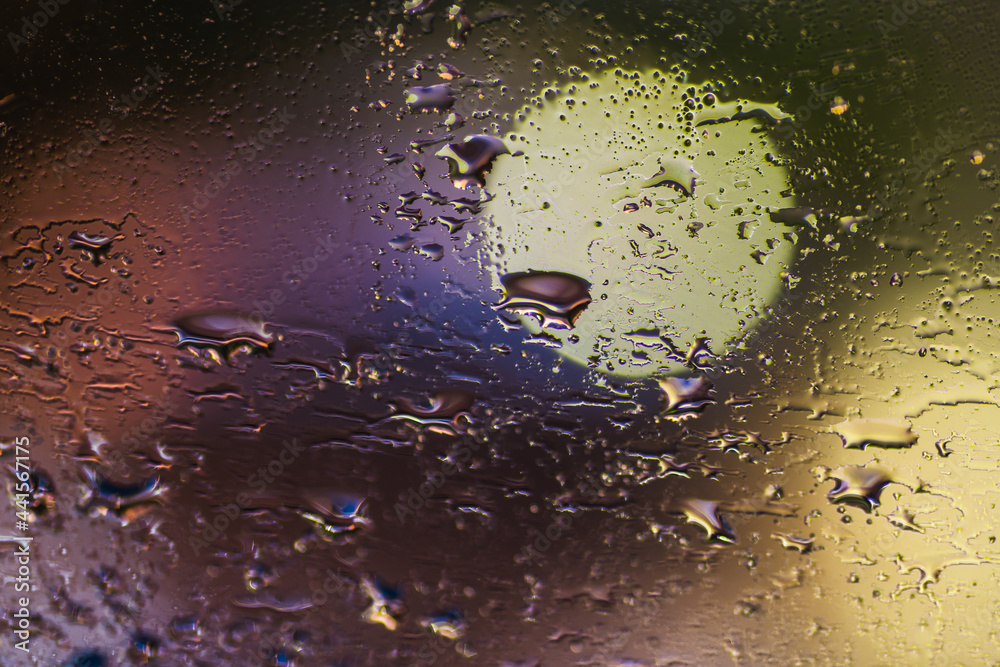Rain drops on window glass at night, moody colorful abstract background.
Rain drops on window glass at night, moody colorful abstract background.
