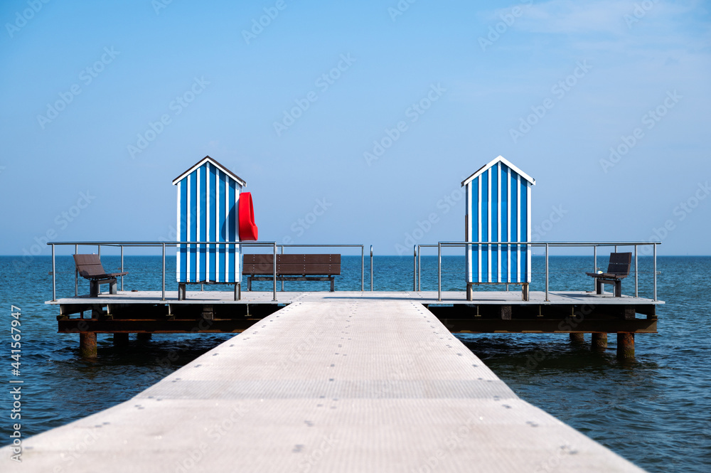 Fototapeta premium End of pier with two wooden houses as changing room and benches on blue sky background