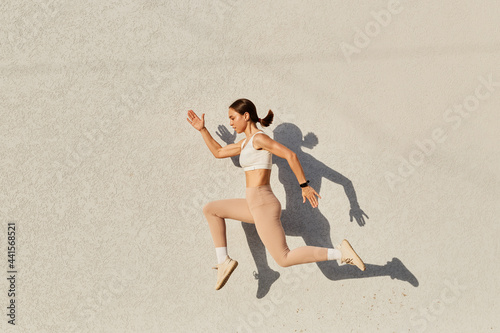 Fototapeta Naklejka Na Ścianę i Meble -  Portrait of woman with perfect body jumping over in the air, wearing white top and beige leggins, doing sports exercises outdoor, healthy lifestyle, body care.