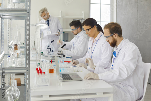 People working in medical laboratory. Group of male and female scientists sitting at lab table with laptop  doing advanced research  using glassware equipment  developing new drug and collecting data