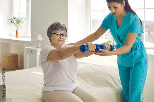 Home care nurse, physician or physiotherapist checks how happy female patient is doing arm rehabilitation exercise. Providing help, physical therapy and wellness workout practice for senior citizens photo