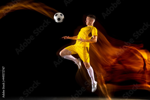 Young caucasian male football or soccer player training in mixed light isolated on dark background. Concept of healthy lifestyle, professional sport, active, motion..