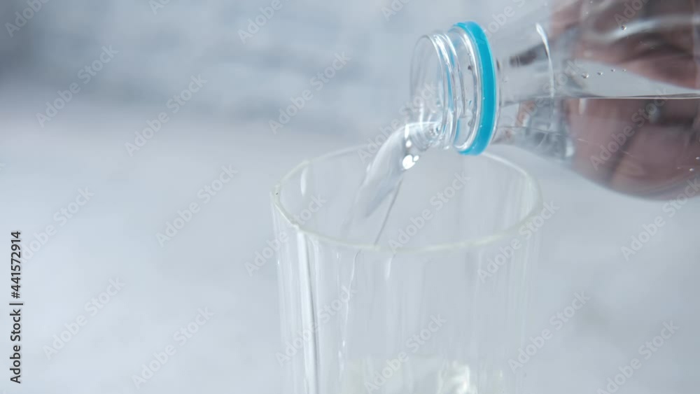 pouring water from a plastic container in a glass on table pouring water from a plastic container in a glass on table