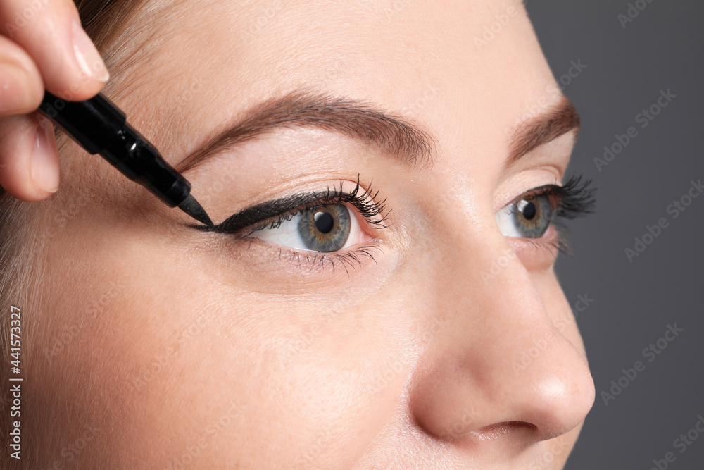 Artist applying black eyeliner onto woman's face on grey background, closeup