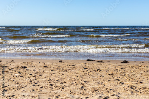 Seashore at Ragakapa Beach in Jurmala, Latvia. Yellow sandy beach where blue Baltic sea waves with white foam are reaching the coast at sunny day. 