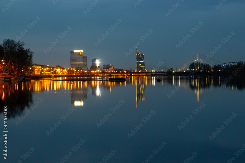 Naklejka premium Night view of the city Riga, Latvia. Blue night photo to the city of Riga when building reflecting in the water of Daugava river.