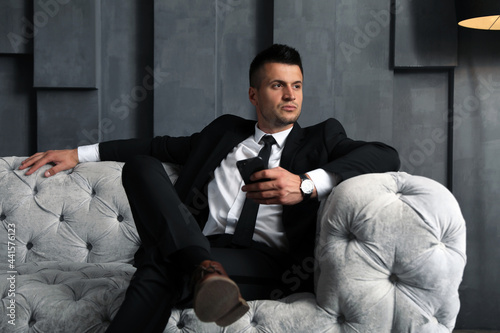 Fotografie Handsome businessman with smartphone on sofa indoors