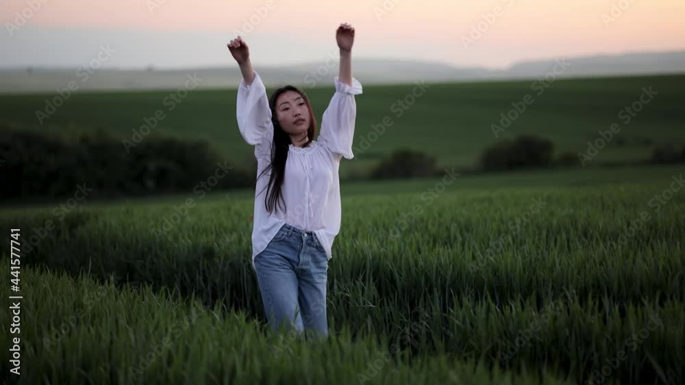 Young asian woman happily walking in slow motion through a field touching with hand wheat ears. Beautiful carefree girl enjoying nature and sunlight in wheat field at incredible colorful sunset Young asian woman happily walking in slow motion through a field touching with hand wheat ears. Beautiful carefree girl enjoying nature and sunlight in wheat field at incredible colorful sunset