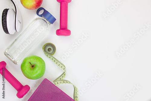 Two red dumbbells, an apple, a tape measure, a bottle of water and weight scales on a white background. Concepts about fitness, sport and health. Copy space for text. Home workout concept