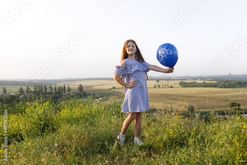 happy girl with red hair and blue dress having fun with an balloon in nature