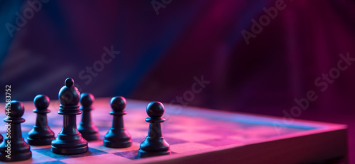 Foto Chess pieces on a chessboard on a dark background shot in neon pink-blue colors