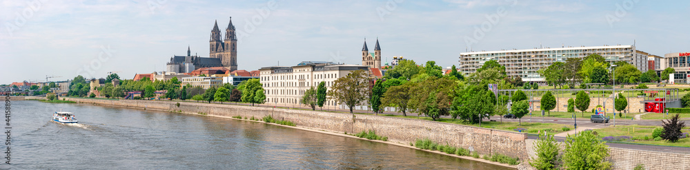 Panoramic view over old cathedral at historical downtown in Magdeburg with a touristic boat coming by at Elbe River, Germany, at blue summer sky with clouds.