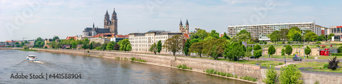 Panoramic view over old cathedral at historical downtown in Magdeburg with a touristic boat coming by at Elbe River, Germany, at blue summer sky with clouds.
