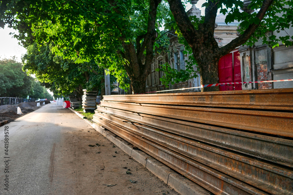 A large pile of stacked rails against the backdrop of road works in the city. Streetcar rails against the background of construction work. Replacement of streetcar tracks in the city.