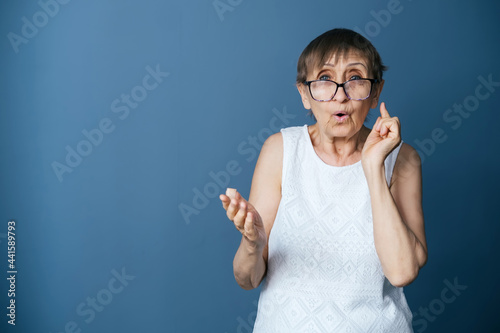 Portrait of elderly woman on gray-blue background  explaining something and looking at the camera through glasses