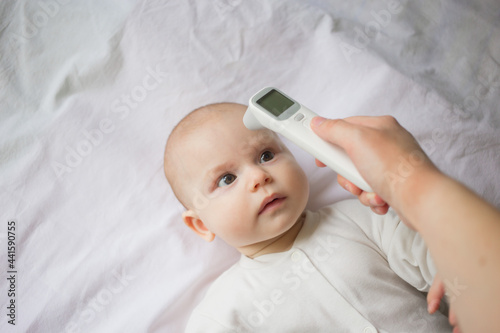 Fever and colds in an infant runny nose, flu or covid.Mom's hand holds a thermometer at the child's forehead and measures his temperature..