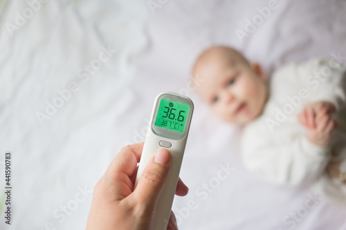 Fever and colds in an infant runny nose, flu or covid.Mom's hand holds a thermometer at the child's forehead and measures his temperature..
