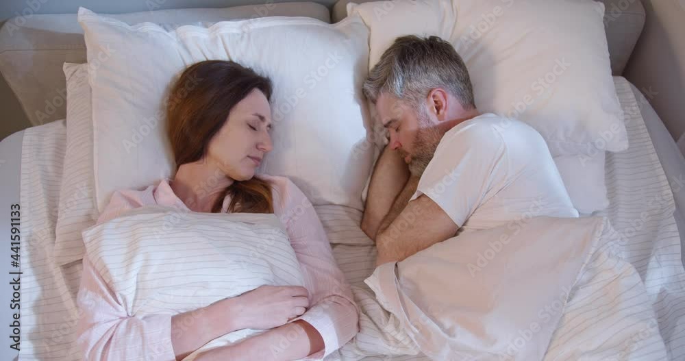 Caucasian adult couple laying at the bed with each other and sleeping. Man and woman continue to sleeping at the morning. Morning and bedroom concept Caucasian adult couple laying at the bed with each other and sleeping. Man and woman continue to sleeping at the morning. Morning and bedroom concept