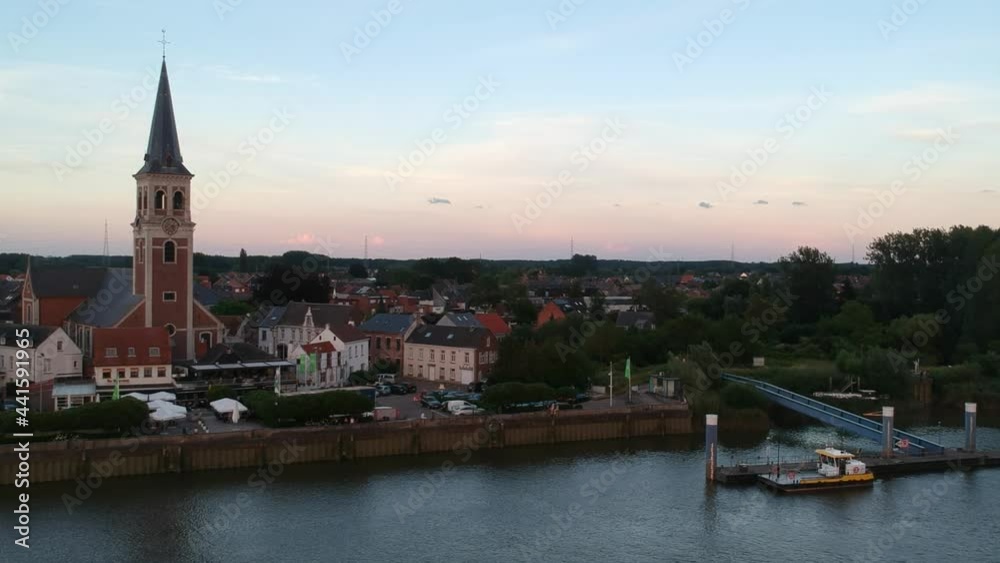 River coastline and pier with small town and church tower, sunset aerial view River coastline and pier with small town and church tower, sunset aerial view