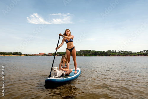 pretty young woman and her daughter paddle boarding with a small dog