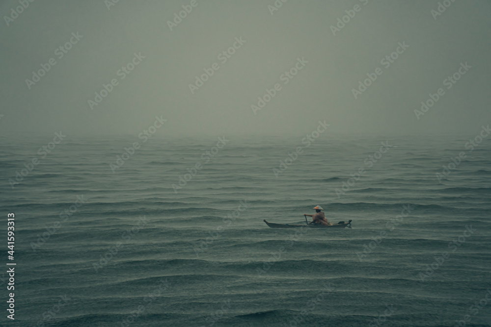 a fisherman and small fishing boat sailing in the middle of the ocean when a rainstorm hit. hard working man and moody landscape concept.