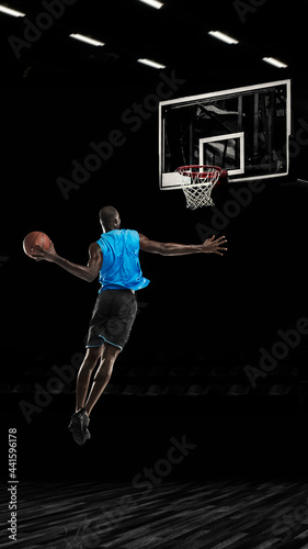 One young sportsman basketball player training in gym, idoors isolated on dark background. Concept of sport, game, competition. Slam dunk © master1305