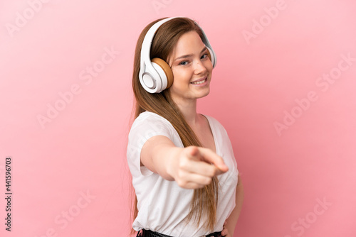 Teenager girl over isolated pink background listening music and pointing to the front
